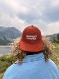 Happiest Camper Hat worn outdoors with mountains in the background, showcasing the embroidered design.