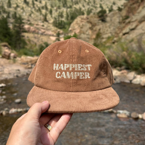 Rustic 'Happiest Camper' corduroy hat by Trek Light, perfect for outdoor adventures. 6-panel snapback, one size fits most.