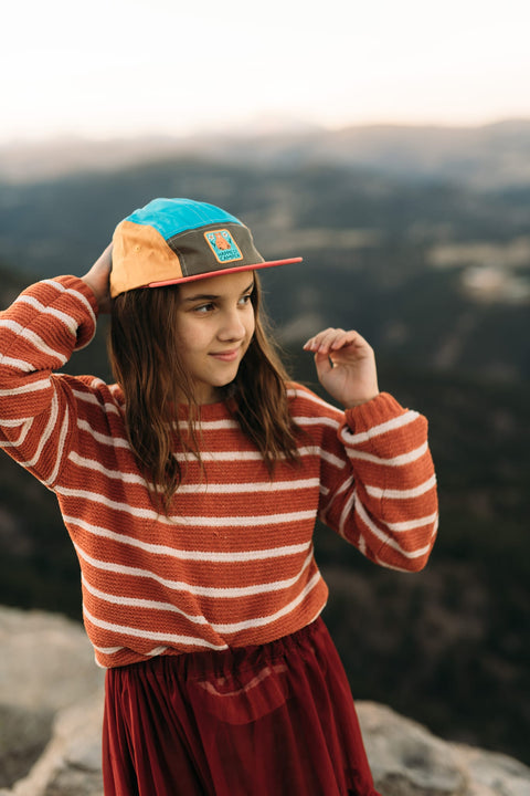 Child wearing Happiest Camper Kids Hat by Trek Light, 5-panel snapback, flat brim, colorful design, outdoors adventure spirit.