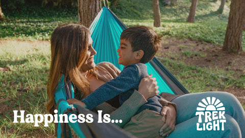 Mother and child relaxing in a Trek Light hammock, enjoying a sunny day in the forest.
