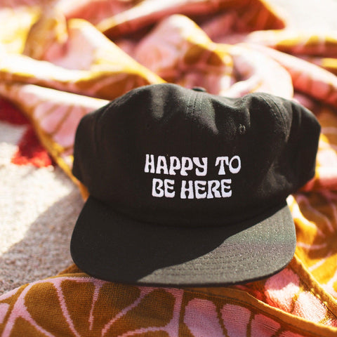 Trek Light "Happy To Be Here" hat on colorful fabric, expressing joy and outdoor vibes.