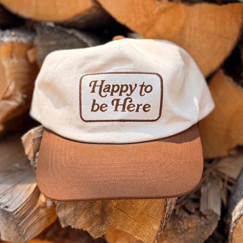 Happy To Be Here Hat resting on wooden logs with a captivating design, ideal for style and comfort.