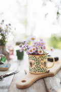 Honey Bee Enamel Mug 16oz filled with flowers on a wooden surface, perfect for adding charm to your mornings.