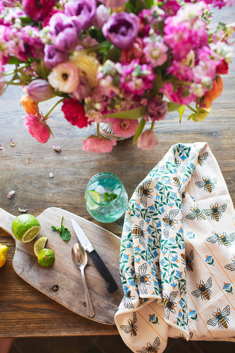 Honey Bee Kitchen & Tea Towel on a wooden table with limes, knife, and a glass of drink.