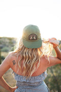 Woman wearing Howlin' At The Moon Hat against a sunset backdrop, showcasing style and comfort.