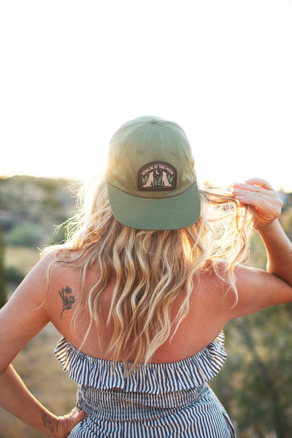 Woman wearing Howlin' At The Moon Hat against a sunset backdrop, showcasing style and comfort.