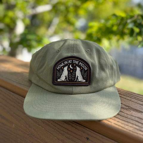 Trek Light Howlin' At The Moon Hat on wooden ledge with forest background, perfect for adventurous spirits and wild howlers.