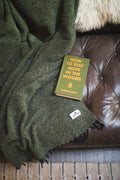 Cozy Humboldt Blanket draped over a leather couch with 'How to Stay Alive in the Woods' book, handwoven and eco-friendly design.