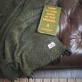 Cozy Humboldt Blanket draped over a leather couch with 'How to Stay Alive in the Woods' book, handwoven and eco-friendly design.