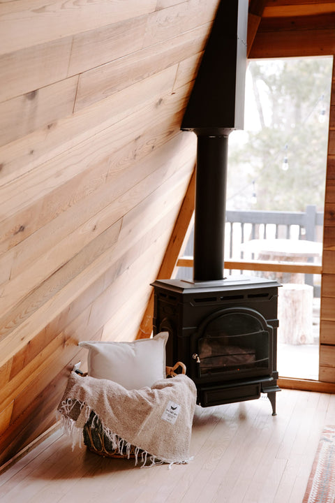 Cozy Huntington Blanket by Trek Light near a wood stove in a rustic cabin setting, perfect for beach or campfire nights.