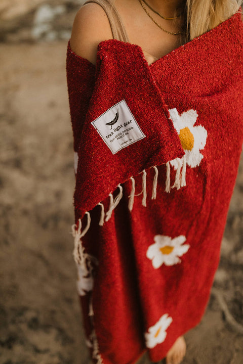 Cozy Lazy Daisy Blanket by Trek Light, wrapped for comfort and relaxation, featuring charming daisy patterns on lush red fabric.