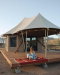Woman lounging on a Lazy Daisy Blanket in front of a glamping tent at sunset.