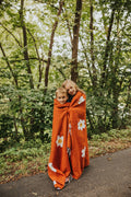 Kids wrapped in Lazy Daisy Blanket outdoors, enjoying nature's comfort and warmth with vibrant orange color.