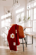 Cozy red Lazy Daisy Blanket on a chair, featuring a charming daisy print. Perfect for slowing down and savoring life's lazy moments. Trek Light.