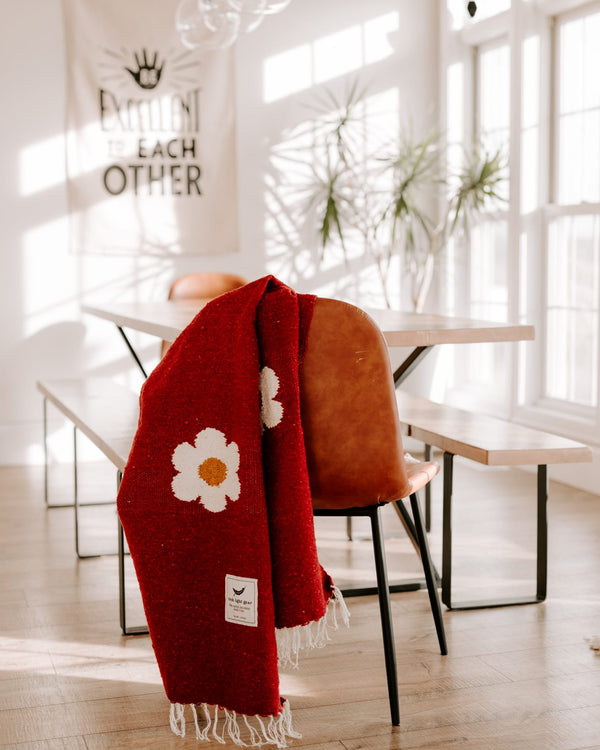 Cozy red Lazy Daisy Blanket on a chair, featuring a charming daisy print. Perfect for slowing down and savoring life's lazy moments. Trek Light.