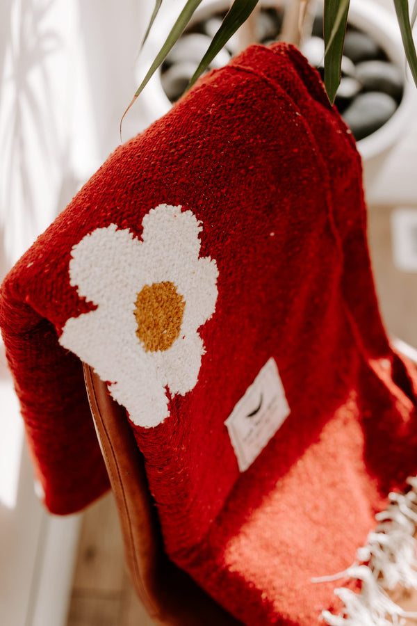 Cozy red blanket with a white daisy design draped over a chair, embodying Trek Light's Lazy Daisy vibe.
