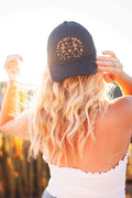 Woman wearing a black Let's Get Weird Hat in sunset, featuring quirky skeleton design and adjustable fit.