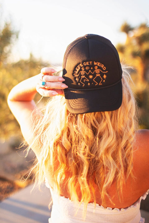 Woman wearing a Let's Get Weird Hat, showcasing its unique design against a sunny backdrop.