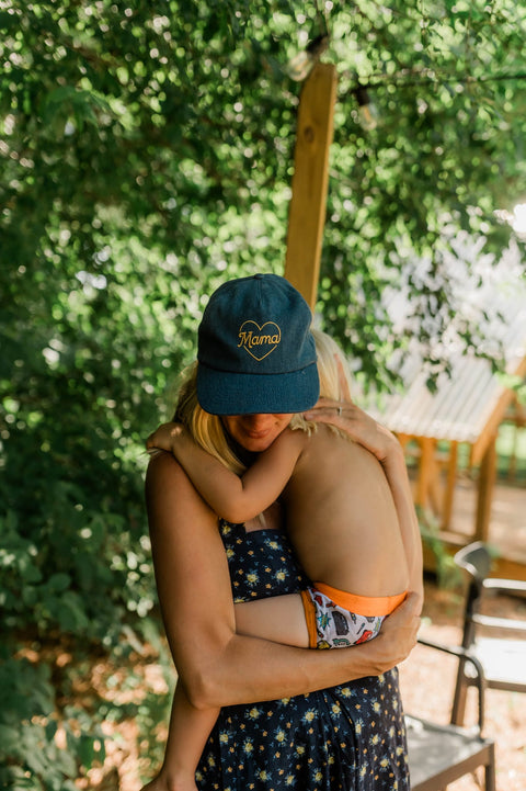 Mama Hat worn by a mother embracing her child in a lush, green setting.