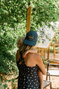 Mama Hat worn by a woman holding a child, showcasing its comfortable design and stylish look.