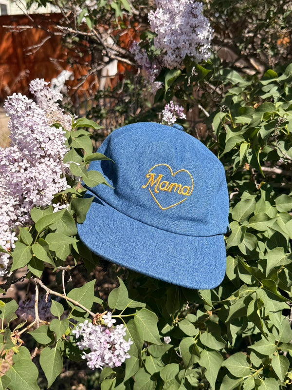 Mama Hat on a bed of lilac flowers, featuring a heart design and adjustable fit for comfort.