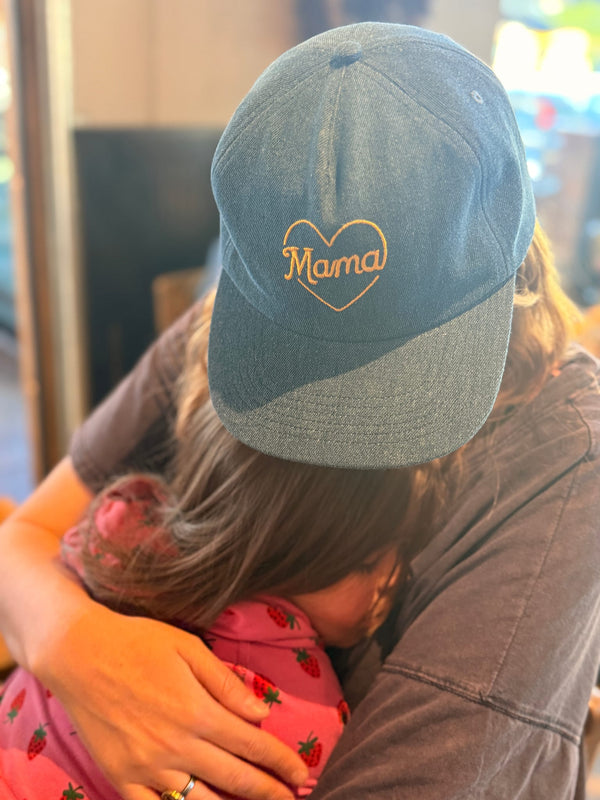 Mama Hat with heart embroidery worn by a person embracing a child, showcasing comfort and style.