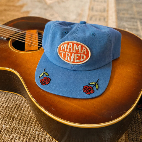 Mama Tried Hat displayed on a guitar, featuring vibrant red roses and an eye-catching logo.
