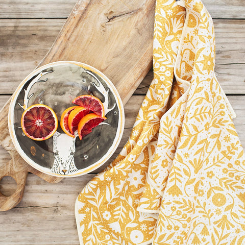 Vibrant Meadow Kitchen & Dish Towel on wooden board beside artistic deer plate adorned with orange slices.