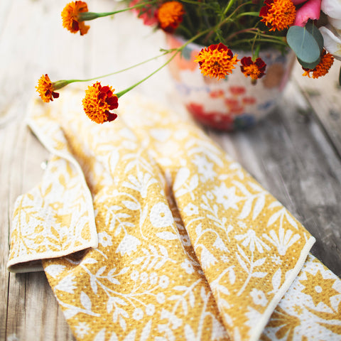 Meadow Kitchen & Tea Towel with vibrant floral design and hanging loop beside a flower pot.