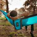 Relaxing in a Trek Light double hammock in nature, perfect for camping or home use, known for stability and comfort.