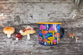 Midnight Mushroom Enamel Mug 16oz featuring vibrant mushroom design against rustic wood background