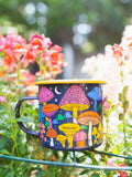Midnight Mushroom Enamel Mug 16oz in a vibrant floral garden setting