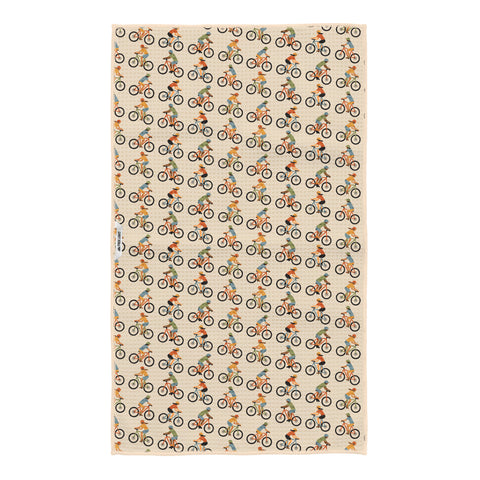 Beige waffle-textured kitchen towel covered in a repeating pattern of colorful illustrated mountain bike riders