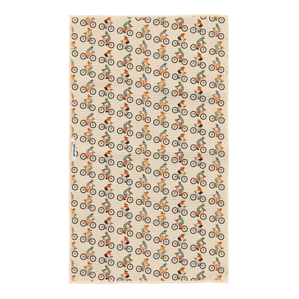 Beige waffle-textured kitchen towel covered in a repeating pattern of colorful illustrated mountain bike riders