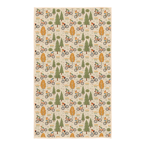 Beige kitchen towel with illustrated mountain bikers riding among green pine trees, aspen trees, and wildflowers