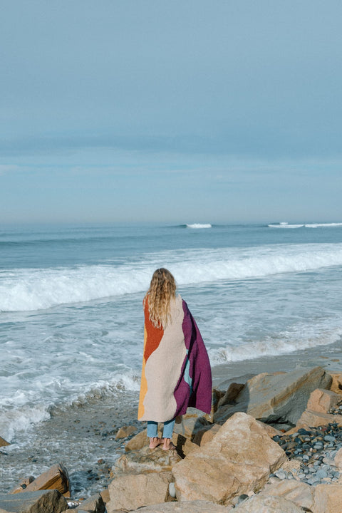 Cozy handwoven Mountain Sunrise Blanket made from recycled materials, perfect for versatility and warmth, by the ocean. By Trek Light.