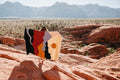 Person holding a colorful handwoven Mountains Blanket by Trek Light, set against a stunning mountain backdrop, made from recycled materials.