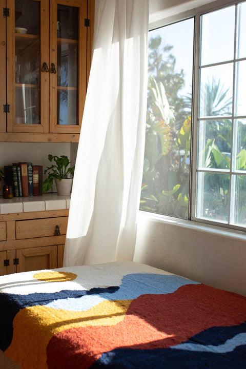 Vibrant handwoven Mountain blanket by Trek Light, capturing sunlight by a window, inviting warmth and artistic flair into your space.