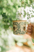 Honey Bee Enamel Mug 16oz with floral design held in hand, perfect for cozy mornings and outdoor adventures.