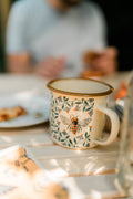 Honey Bee Enamel Mug 16oz resting on a table surrounded by pastries and soft morning light.