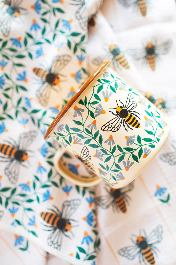 Honey Bee Enamel Mug 16oz with floral design and bees on a tablecloth, perfect for cozy mornings.