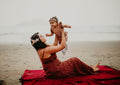 Woman lifting child joyfully on a Napa Blanket on the beach, enjoying a cozy moment together.