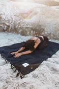 Person practicing yoga on navy Newport Blanket by Trek Light Gear, set on sandy beach.