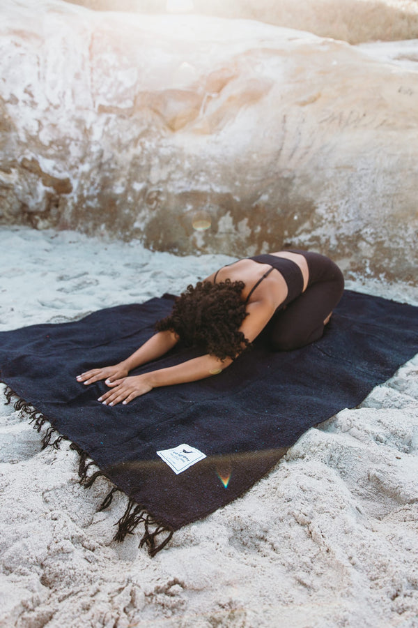 Person practicing yoga on navy Newport Blanket by Trek Light Gear, set on sandy beach.