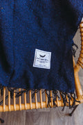 Navy Newport Blanket by Trek Light draped on a chair, perfect for outdoor festivals; embrace music and comfort with style.
