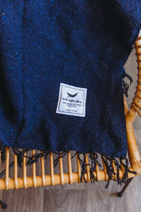 Navy Newport Blanket by Trek Light draped on a chair, perfect for outdoor festivals; embrace music and comfort with style.