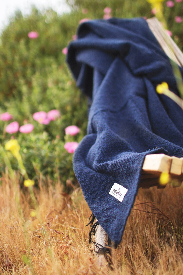 Newport Blanket draped over a bench, surrounded by flowers, emphasizing its coastal charm and eco-friendly design.