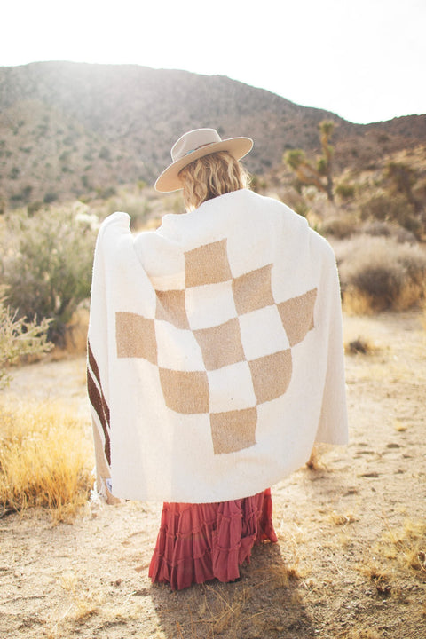Cozy person wrapped in handwoven North Star blanket made from recycled materials, displaying beautiful natural tones and checker pattern. By Trek Light.
