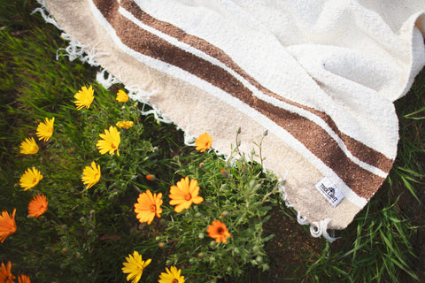 Beautiful handwoven North Star blanket made from recycled clothing materials, draped on grass with yellow flowers, cozy and versatile. By Trek Light.