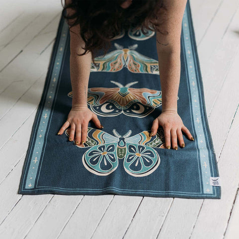 Woman doing yoga on a beautifully designed mat featuring moth illustrations by Trek Light. Calm and creative workout space.